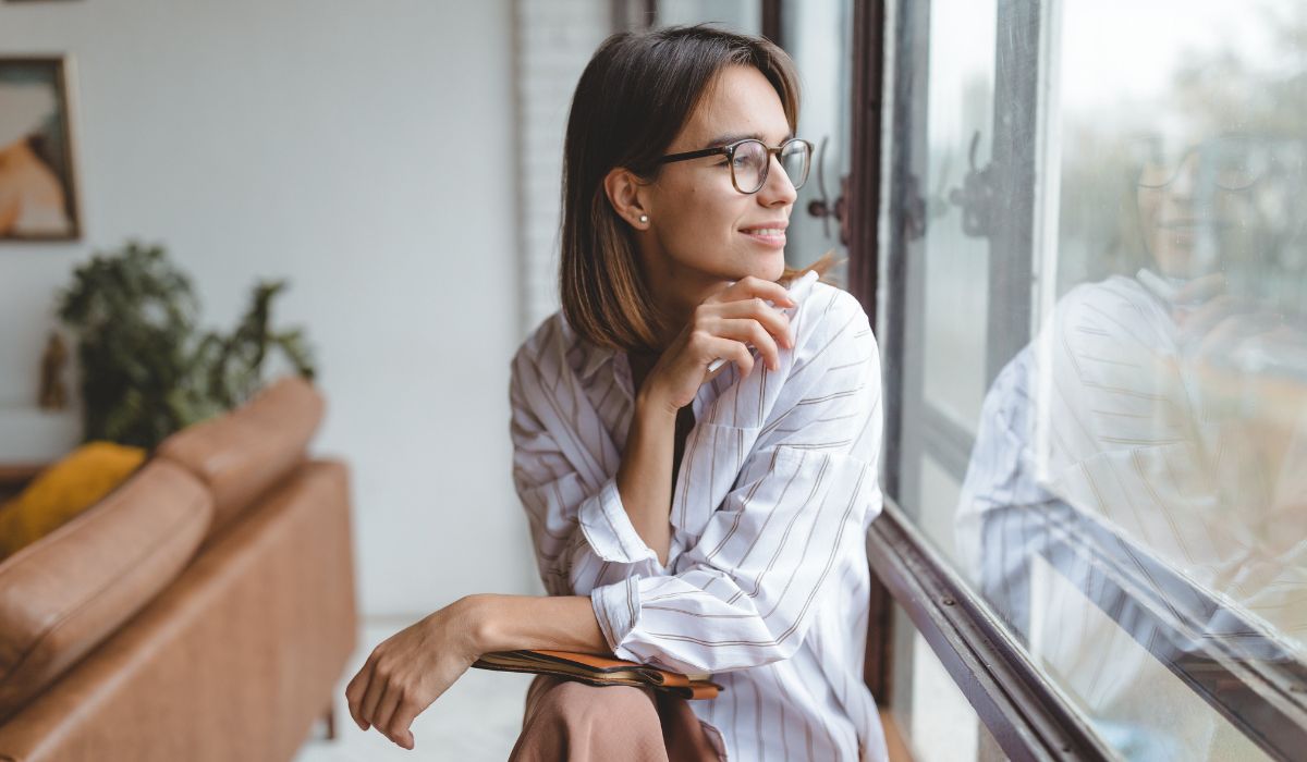 Woman looking out window, pondering the future of mental health.