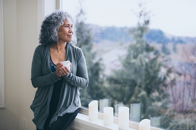old woman holding a coffee mug sitting on the window ledge